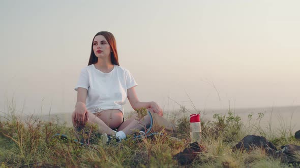 Young Pregnant Woman Sits on Yoga Mat in Lotus Position and Looks at Camera Background Sky Front