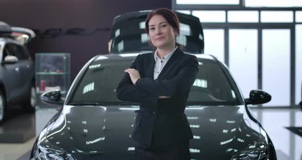 Portrait of Adult Successful Female Car Dealer Posing in Dealership. Caucasian Brunette Woman