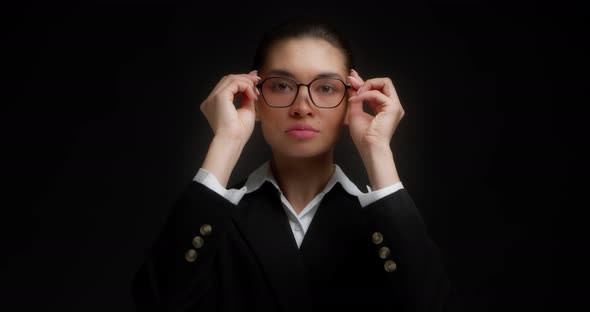 Beautiful Businesswoman Puts on Glasses on Black Background