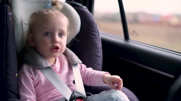 Little girl in a child seat looks out the window while driving a car