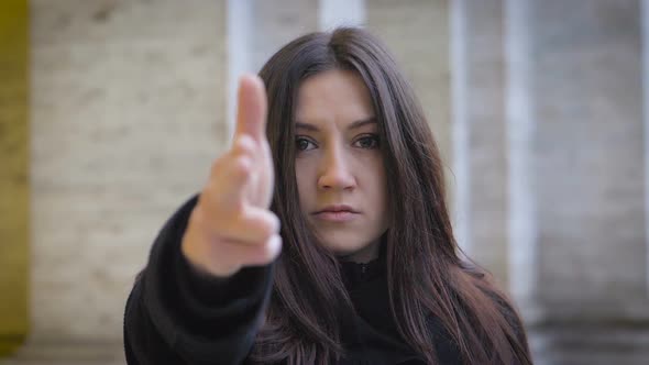 Serious confident young woman making gun gesture with hands at camera