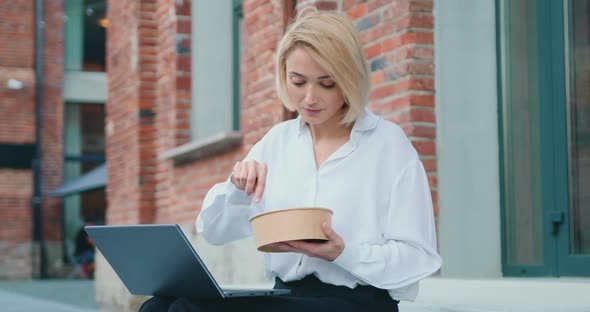 Woman Having a Lunch with a Salad While Sitting on the Stairs with a Laptop.