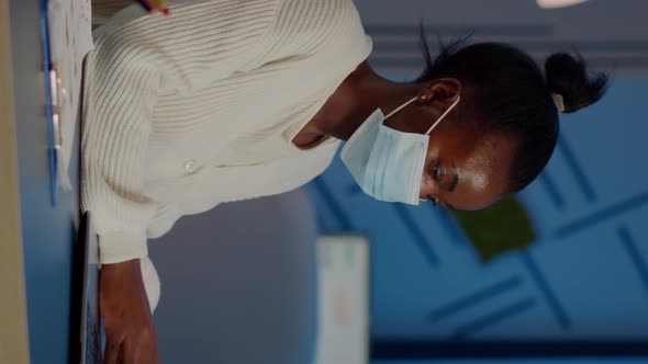 African Employee with Protection Face Mask Working at Laptop Overtime