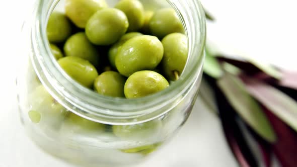 Jar with green olives and olive leaves