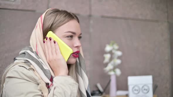 woman with a scarf on her head sits on the street and talks on the phone