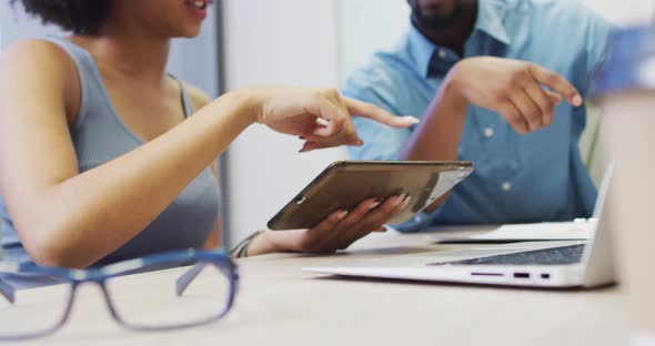 Video of midsection of diverse businessman and female designer working with tablet