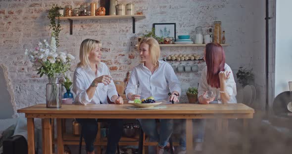 Young Women Girlfriends are Sitting at a Table in a Cozy Kitchen and Talking