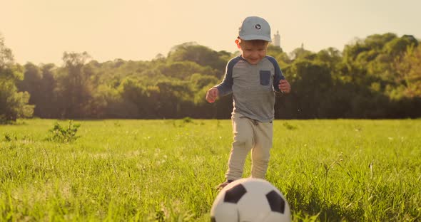 The Boy Runs with a Soccer Ball Laughing at the Sunset in Slow Motion