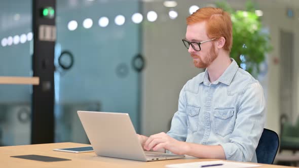 Excited Casual Redhead Man Celebrating Success on Laptop in Office 