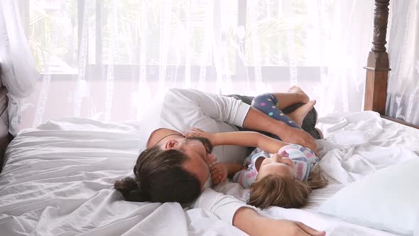 Happy Family Idyll Little Child Daughter Jump On Father Arms And They Fall On A Bed