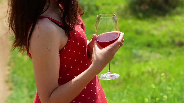 A woman in a red dress with polka dots in nature holds a glass of red wine in her hand