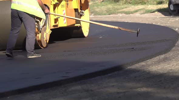 Road Repair. Asphalt Laying. Worker Levels the Newly Laid Road Surface and the Roller Makes the