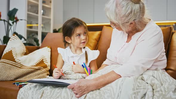 Grandmother and Granddaughter Talking and Smiling Drawing with Felttip Pens on a Sheet of Paper