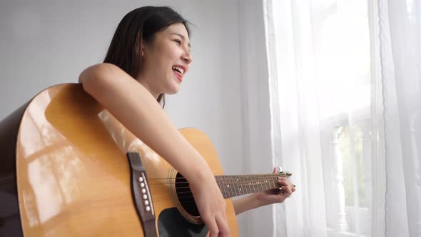 Cheerful Pretty Woman singing and play guitar in bedroom
