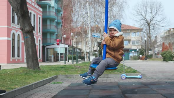 A Boy on a Playground in an Autumn Park Rides on a Swing in Cloudy Weather