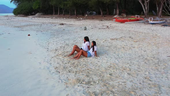 Girls tanning on paradise lagoon beach voyage by blue green water and white sandy background of Lomb