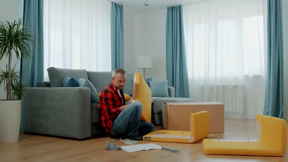 A Man at Home in the Living Room Assembles a Yellow Lounge Chair