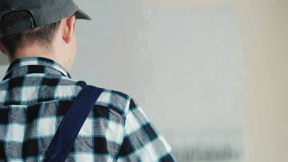 Male Builder Paints Wall with Roller. Rear View alt