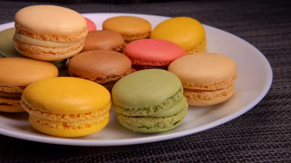 Hands Are Taking Multi-colored French Almond Macaroons From the White Plate