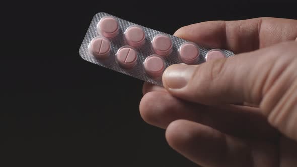 Man's Hand Holds Tablets in a Package on a Dark Background. Coronavirus, Pandemic. Close Up