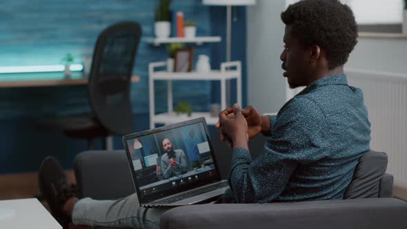 Black Man Unsing Laptop for Online Internet Conference Chat with His Coworkers