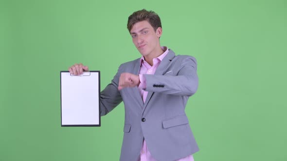 Stressed Young Businessman Showing Clipboard and Giving Thumbs Down