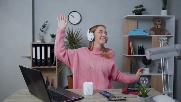 Young Girl in Stylish Sweater Sitting at the Table and Using Headphones and Her Phone