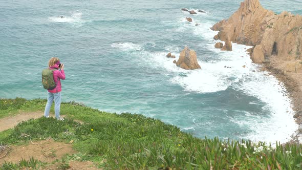 Joyful Girl Photographer Takes Picture of Ocean From Cliff