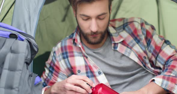 Close Up of Young Man Drinking Hot Coffee After Hiking. Beautiful Man Relaxing in a Tent. Camping