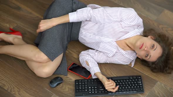 Tired Young Female Office Manager is Lying on the Floor with Keyboard Mouse and Smartphone Lay Flat