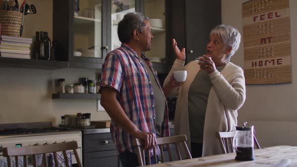 Happy senior mixed race couple having coffee talking in kitchen