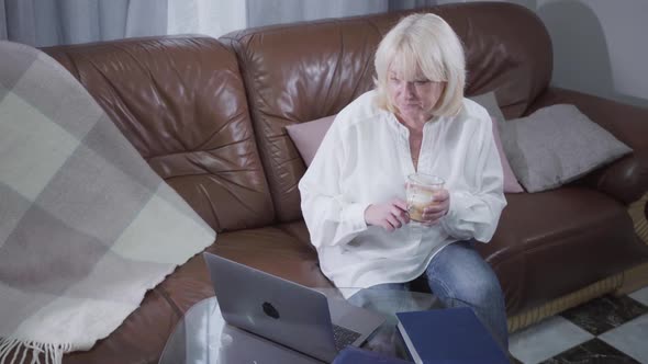 Top View of Mature Caucasian Woman in Casual Clothes Drinking Coffee and Surfing Internet