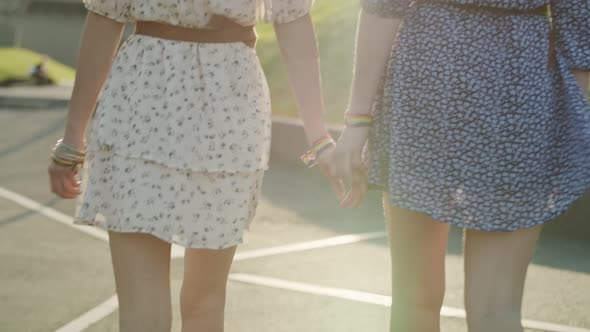 Handheld video of two unrecognizable women walking and holding hands. 