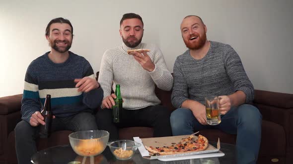 Portrait of Three Nice Attractive Cheerful Cheery Guys Drinking Beer and Watching Comedy on TV