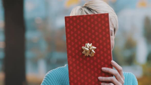 Young Woman Revealing Her Satisfied Face Behind the Gift Box in the Park