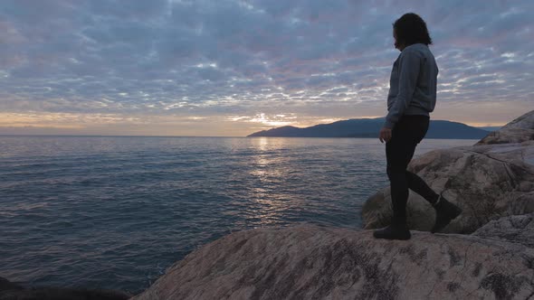 Caucasian Woman on a Rocky Coast During a Dramatic Cloudy Sunset