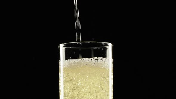 Sparkling Yellow Water is Pouring Into Wineglass Standing on Black Background