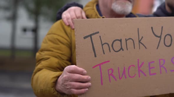 Two Adult Men Stand Embracing with a Poster Thank you Truckers