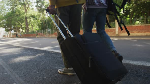 Low section of two mixed race male friends walking with suitcase down the street