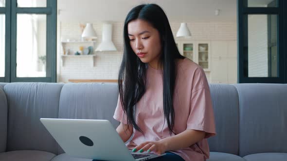 Young Thoughtful and Pensive Woman of Asian Ethnicity Working on Laptop Typing Text Looking Around