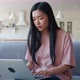 Young Thoughtful and Pensive Woman of Asian Ethnicity Working on Laptop Typing Text Looking Around - VideoHive Item for Sale
