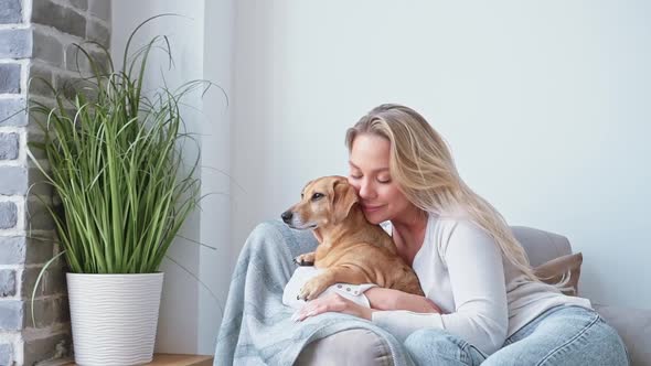 Young Beautiful Blonde Woman Caucasian Nationality Home Clothes Sits in a Cozy Armchair Hugging Her