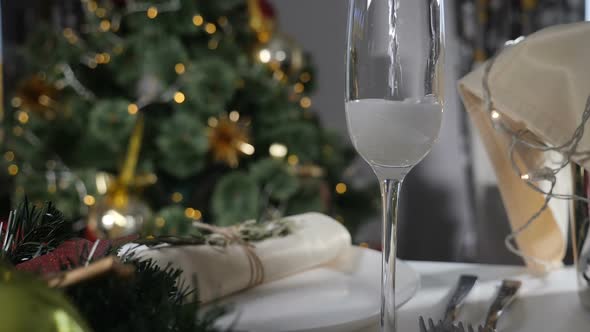 New Year Holiday. Champagne Being Poured Into Glass on Decorated Feast Table and Christmas Tree with