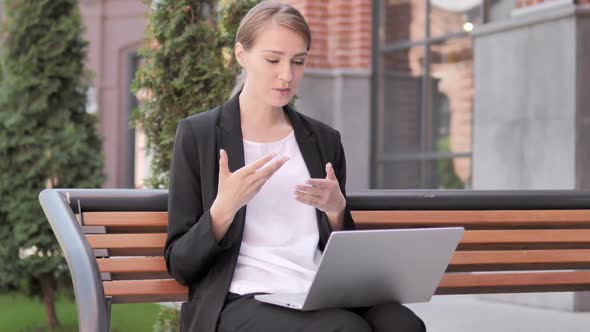 Online Video Chat on Laptop By Young Businesswoman Sitting on Bench