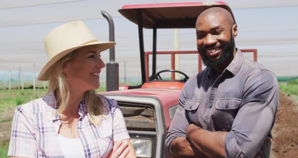 Video of happy diverse man and woman standing in front of tractor