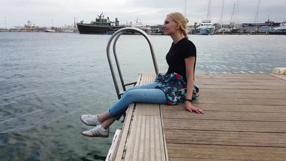Beautiful Girl Sits on the Background of Yachts and Boats Moored in the Port of the Resort Town
