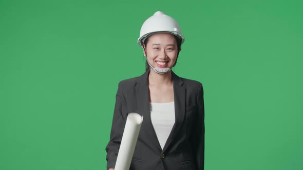 Smiling Asian Female Engineer With Safety Helmet And Blueprint Walking In The Green Screen Studio