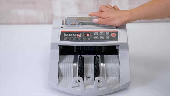 USD on money counting machine. Woman putting money into counting machine