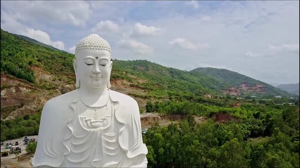 Flycam Approaches Closely To Buddha Statue Head Against Hill