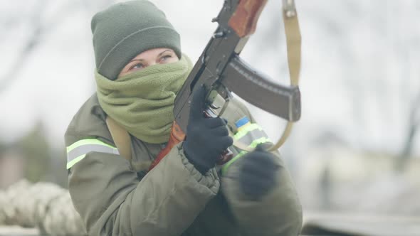 Masked Female Caucasian Soldier Reloading Gun and Aiming Lying on Outdoor Polygon